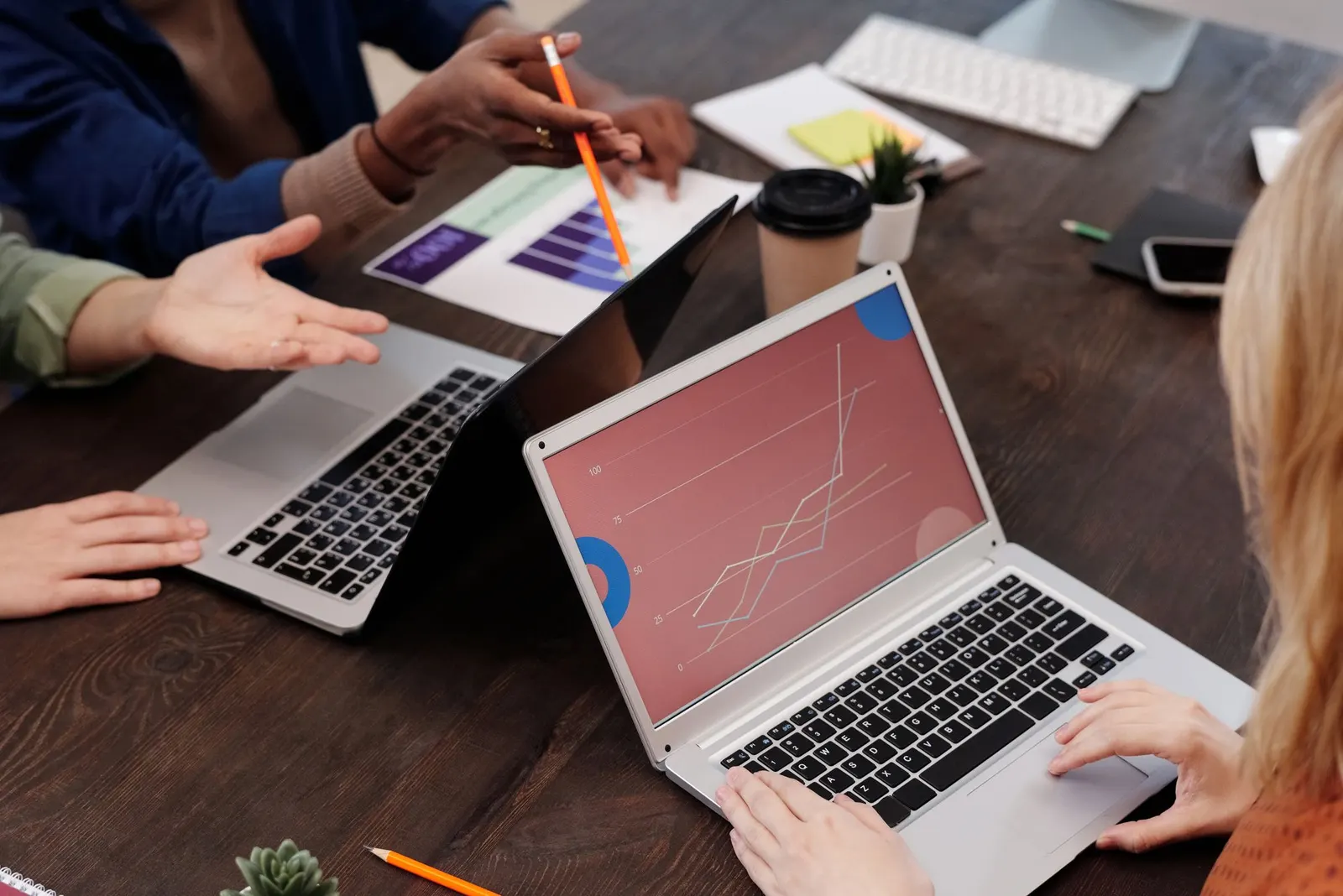 Colleagues at a dark table reviewing charts on two laptops with pens and notebooks