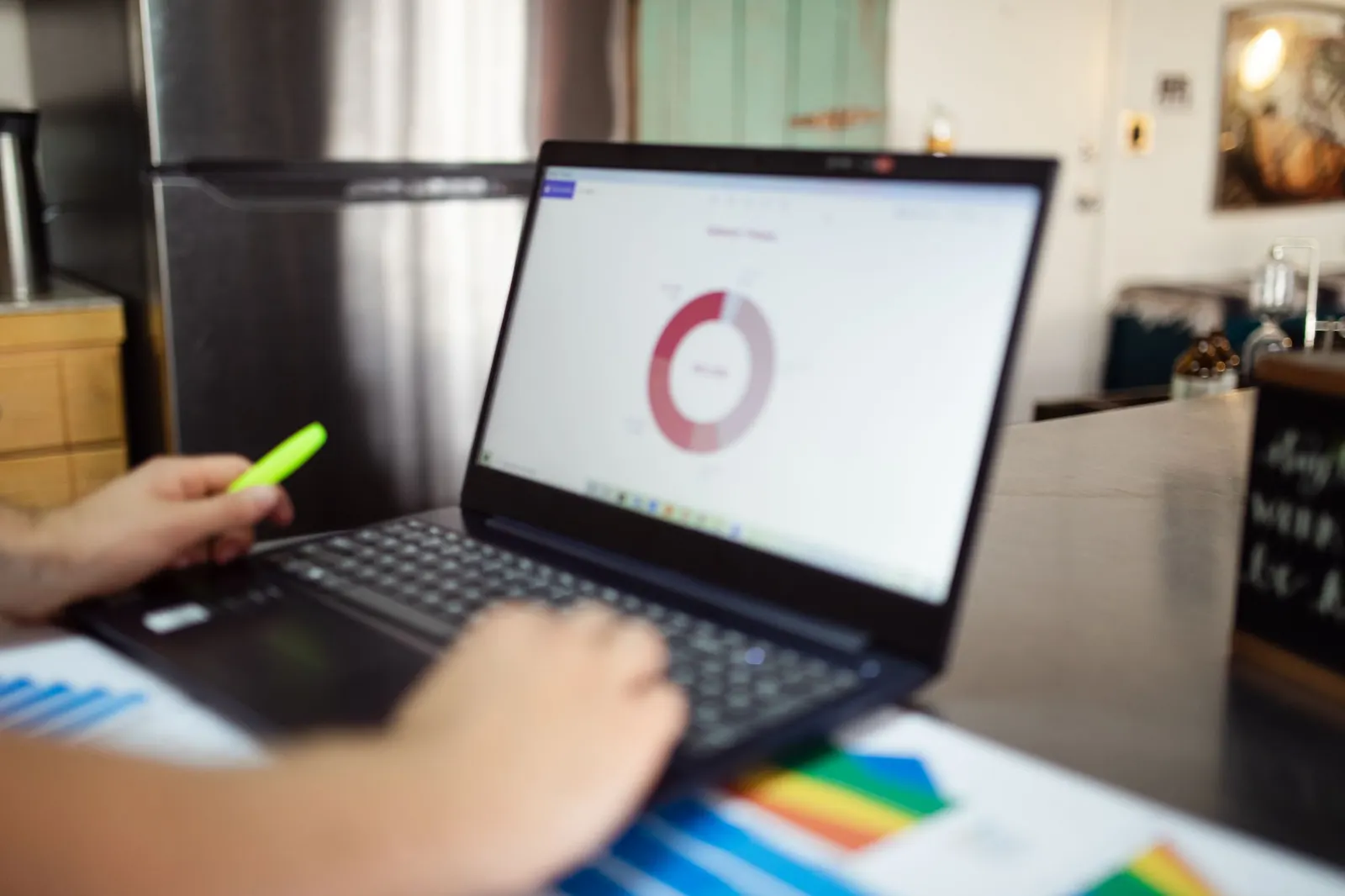 Laptop screen showing a donut chart with a person holding a highlighter over colorful printed reports