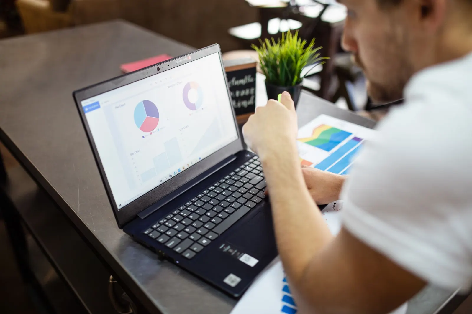Person working on a laptop showing pie and donut charts with colorful printed reports on the desk