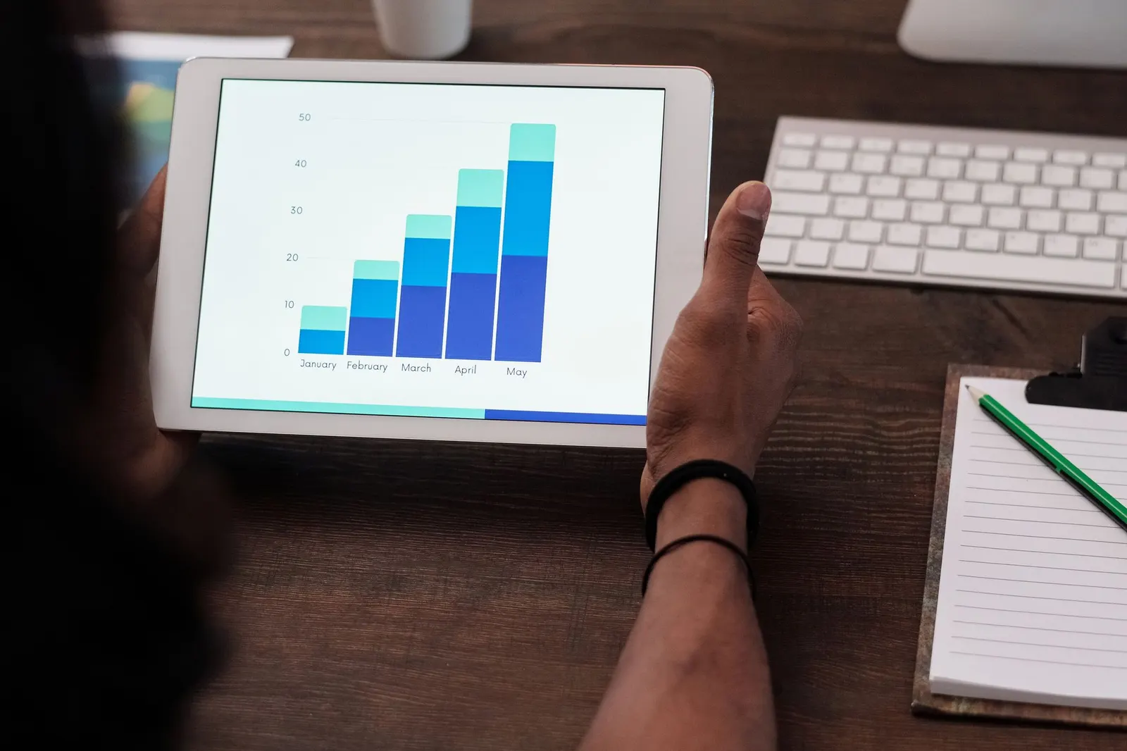Tablet displaying a blue bar chart held over a desk with a keyboard and notebook