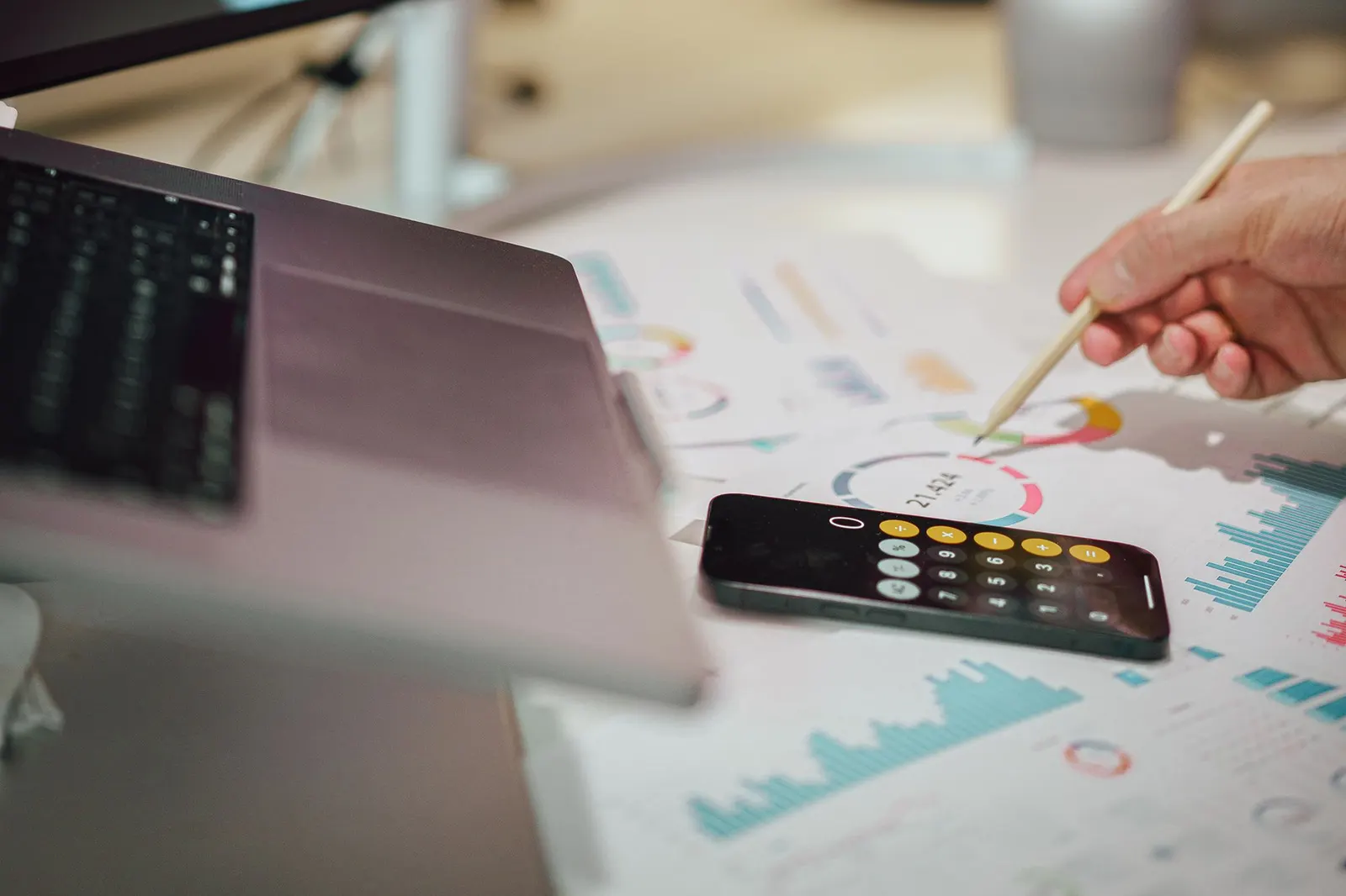 Analyst marking printed charts with a pencil next to a laptop and a calculator