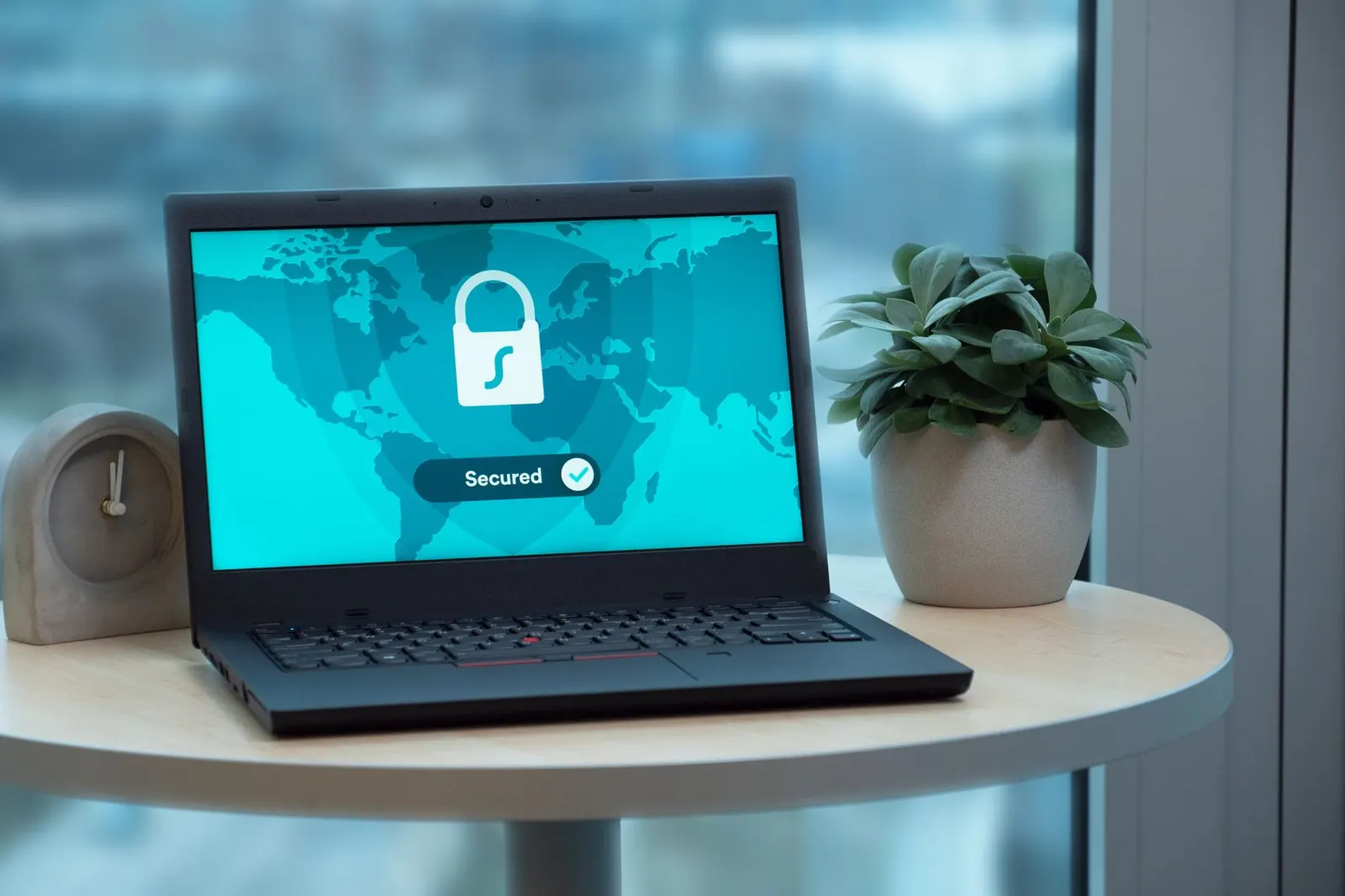 Laptop on a round table displaying a padlock icon and the word secured on a teal world map